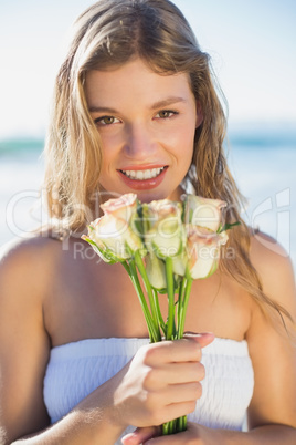 Beautiful blonde in sundress holding roses on the beach