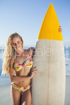 Gorgeous blonde surfer in bikini holding her board