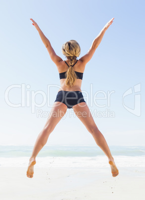 Fit blonde jumping on the beach with arms outstretched