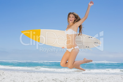 Smiling surfer girl holding her surfboard and jumping on the bea