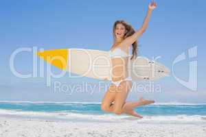 Smiling surfer girl holding her surfboard and jumping on the bea