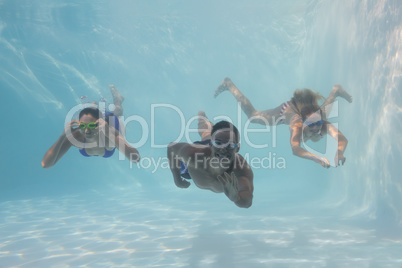 Smiling friends looking at camera underwater in swimming pool