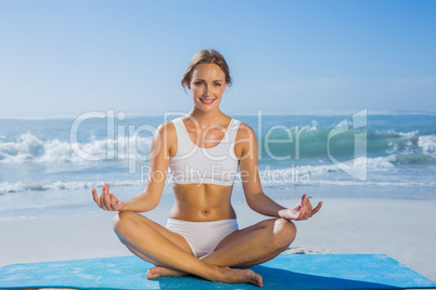 Fit smiling woman sitting in lotus pose on the beach