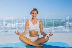 Fit smiling woman sitting in lotus pose on the beach