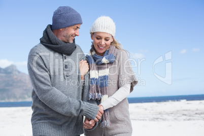 Smiling couple standing on the beach in warm clothing