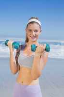 Sporty happy blonde lifting dumbbells on the beach