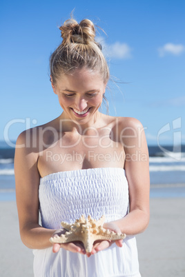 Pretty blonde in white dress holding starfish on the beach