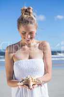 Pretty blonde in white dress holding starfish on the beach