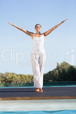 Happy brunette standing poolside with arms raised