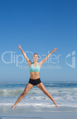 Fit woman jumping on the beach with arms out