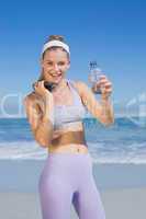 Sporty happy blonde standing on the beach with water bottle and