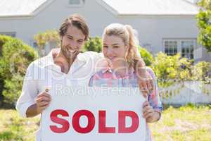Cute couple standing together in their garden holding sold sign