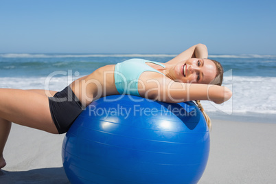 Fit woman lying on exercise ball at the beach stretching