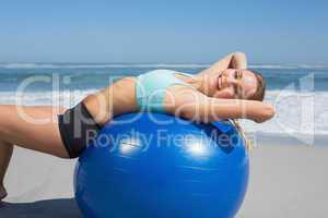 Fit woman lying on exercise ball at the beach stretching