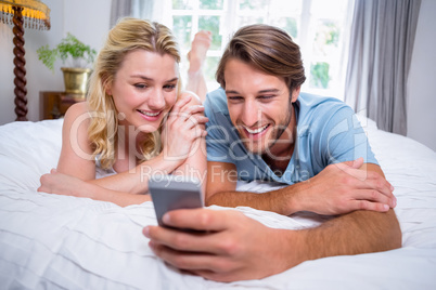 Cute couple relaxing on bed looking at smartphone together