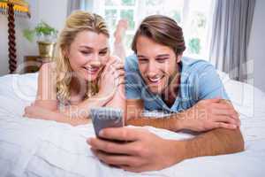 Cute couple relaxing on bed looking at smartphone together