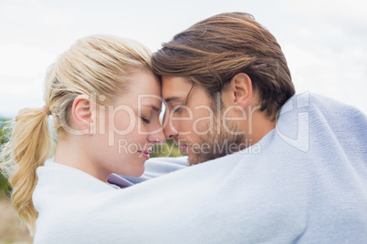 Cute affectionate couple standing outside wrapped in blanket