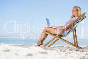 Pretty blonde sitting on beach using her laptop