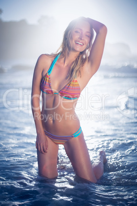 Happy blonde kneeling by the sea posing in bikini