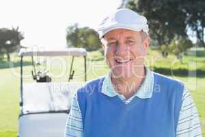 Happy golfer smiling at camera with golf buggy behind