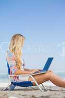 Pretty blonde sitting on beach using her laptop