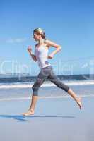 Focused fit blonde jogging on the beach barefoot