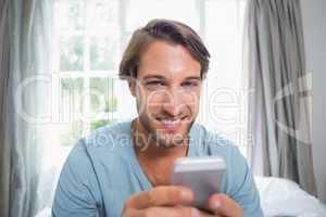Handsome man sitting on bed sending a text message