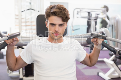 Fit man using weights machine for arms looking at camera