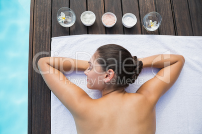 Tranquil brunette lying on towel poolside with beauty treatments