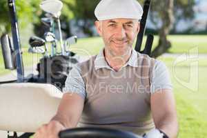 Happy golfer driving his golf buggy smiling at camera