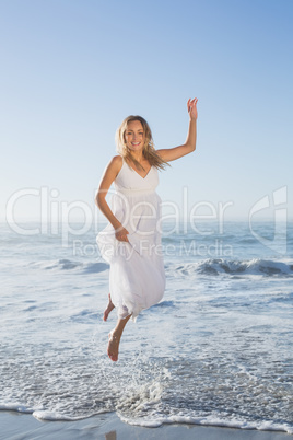 Pretty blonde jumping at the beach in white sundress