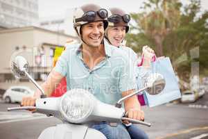 Hip young couple riding scooter with shopping bags