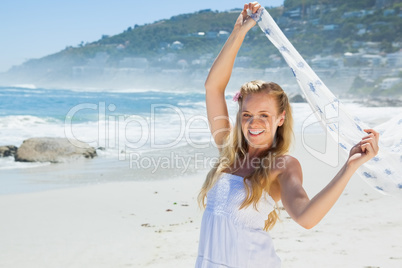 Pretty carefree blonde smiling at camera on the beach with scarf