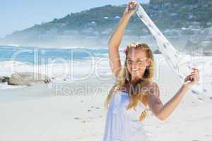 Pretty carefree blonde smiling at camera on the beach with scarf