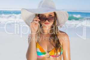 Beautiful girl in bikini and straw hat looking at camera on beac