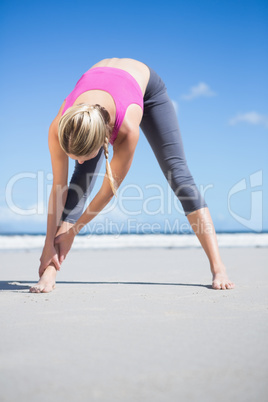 Focused fit blonde warming up on the beach