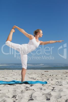 Blonde woman standing in warrior pose on beach