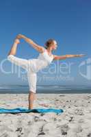 Blonde woman standing in warrior pose on beach