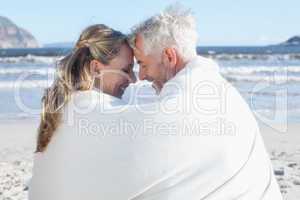 Couple sitting on the beach under blanket smiling at each other