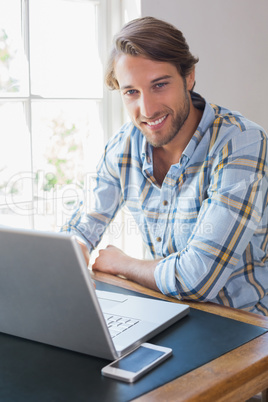 Smiling casual man using laptop looking at camera