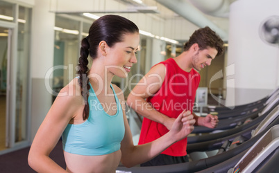 Fit happy couple running together on treadmills