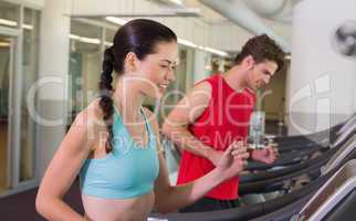Fit happy couple running together on treadmills