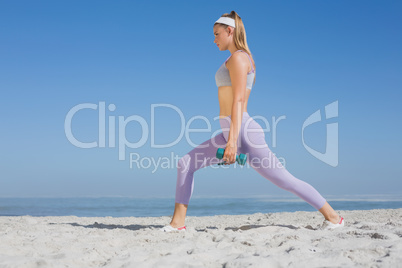 Sporty blonde doing weighted lunges on the beach
