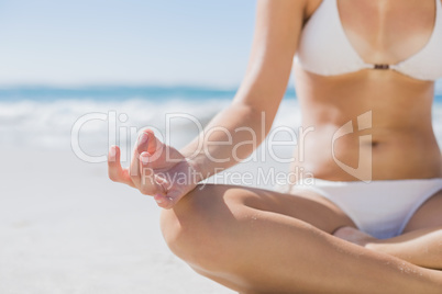 Girl in white bikini sitting in lotus pose on beach