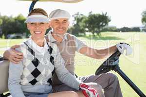 Happy golfing couple driving in their buggy smiling at camera