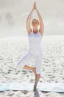 Calm woman standing in tree pose on beach