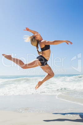 Fit blonde jumping gracefully on the beach