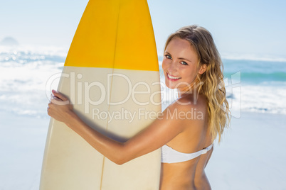 Smiling blonde surfer in white bikini holding her board on the b