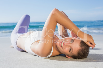 Sporty blonde lying on the beach smiling at camera