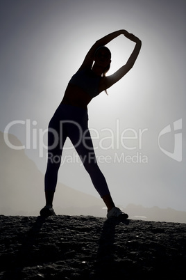 Sporty blonde stretching on the beach on a rock